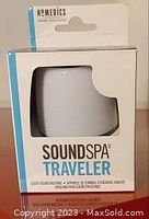 Photo of HoMedics SoundSpa Traveler in original retail box showing white device through clear window with branding and product name.
