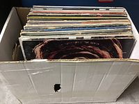 Cardboard box filled with approximately 35 vinyl records showing top edges of album sleeves, varied condition