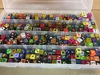 Clear plastic organizer case with four rows filled with approximately 500 small specialty gaming dice in various colors and with numerous fantasy-themed symbols on each die face.