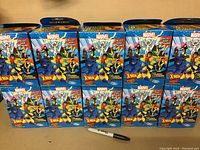 Photo of 10 Marvel Heroclix Colossal X-Men figures in their original boxes arranged in two rows of five, with a pen for scale.