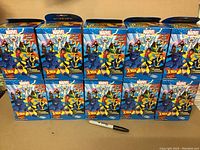 Photo showing 10 sealed boxed Colossal-sized Marvel Heroclix X-Men figures arranged in two rows with a marker for scale.