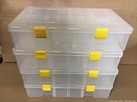 Stack of four clear plastic Plano storage cases with yellow latches, showing uniform size and design.
