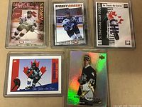 Full view of five Sidney Crosby hockey cards in protective sleeves, showing variety in card editions and holographic effects.