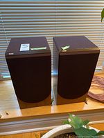 Front view of both speakers side by side on a windowsill with a coil of speaker wire to the right