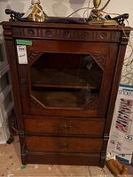Front view of the antique wood cabinet showing glass door, interior shelf, and two drawers with metal handles.