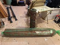 Rolled narrow runner carpet on wooden floor, plastic-wrapped and tied with green string; cleaning tag visible