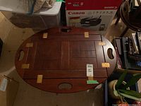 Top view of the wooden coffee table showing oval shape folding top with three handle cutouts and brass hinges.