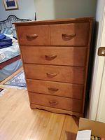 Front view of a light brown wood dresser with five drawers, shows curved wooden handles and minor surface wear.