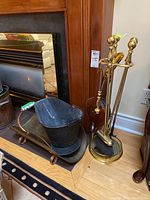 Overall view of fireplace tools set including wood basket and bellows beside fireplace.