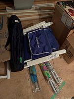 Photo showing two Eddie Bauer blue folding beach chairs stacked with Ozark Trail black folding chair in carry bag and three colorful beach umbrellas below.