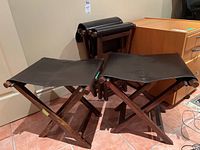 Three folding stools front view, one folded behind, showing dark wood X-frame and leather seats