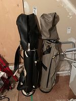 Two upright style golf bags, one black and one beige with black trim, standing side by side.