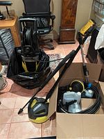 Full view of the Karcher electric power washer unit, surface cleaner attachment on floor, and boxed accessories including hoses and cleaning liquids.