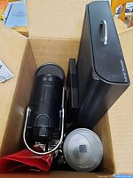 Closed box containing a black Nespresso C60 coffee maker, black capsule holder, coffee capsule recycle bag, and Nespresso menu booklet.