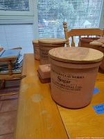 Four Northern Clay Works containers displayed on a wooden table; the one in front is labeled sugar with a wooden lid.