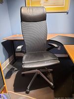 Full view of the office chair showing mesh backrest, leather seat and headrest, and armrests in a corner office setting.
