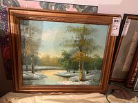 Framed oil painting on stretched canvas showing a winter landscape with snow and trees, in a golden carved frame