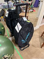 Photo of the black UltimateRebound partial trampoline kit standing upright in its black carrying case with handle and wheels in a room with carpet.