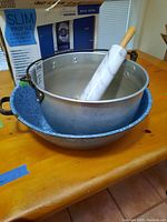 Photo showing the two deep metal pans stacked with the marble rolling pin resting inside the top aluminum pan. Blue speckled enamel pan on bottom, aluminum pan on top with riveted handles.