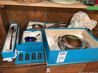 Photo showing various silver plated serving pieces in blue boxes on wooden surface including a covered serving dish, bowl, salt and pepper shakers, and serving spoon.