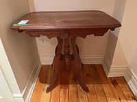 Front view of the wooden side table showing the carved apron and central turned spindle support.