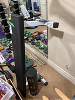 Side view of black padded weight bench and fitness roller on carpeted floor with various weights and gym equipment in background.