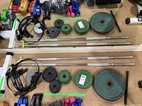 Full lot overview showing barbells, various weight plates, push-up grips, and other small fitness accessories arranged on a carpeted floor.