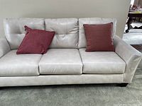 Front view of off white leather couch with red pillows revealing overall condition and style.