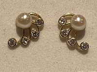 Close-up photo of the front of the earrings showing the pearl and crystals in a gold setting on fabric background.