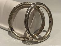 Two silver bangles standing against white background, showing hammered and engraved patterns.