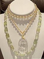 Two beaded jade necklaces on a display bust. One features rectangular light green jade beads, the other a clear carved Buddha pendant with small beads.