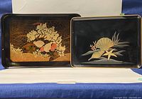 Two Japanese Bakelite trays side by side showing detailed traditional painted designs on black surface.