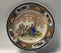 Full view of the round ceramic plate with a detailed painted scene and decorated border.