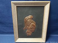 Front view of framed copper metal wall art depicting a woman's face profile.