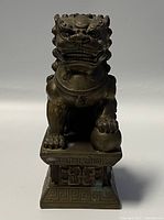 Front view of bronze Foo Dog sculpture showing the head, facial details, and paw on ball.