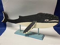 Front and side angled views of the black and white orca carving on light blue stand showing detailed painting and textured body with fins and tail.