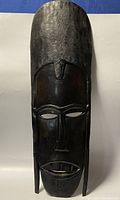 Front view of the tall, wooden tribal mask showing polished dark wood and detailed facial features with textured top section.