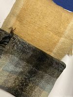 Two mohair rugs layered, showing golden colored Italian rug partially and plaid Scottish rug beneath.