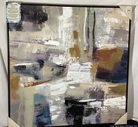Framed abstract canvas art print showing black, white, blue, and brown abstract shapes with textured acrylic embellishments.