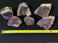 Overview of six amethyst geode specimens arranged with measuring tape for scale, showing varying sizes and purple crystal clusters on rock matrix under fair condition.