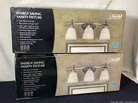 Two boxed Feit Electric Energy Saving Vanity Fixtures, sealed in original packaging with detailed product specifications.