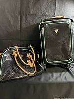Photo showing the full Guess luggage set with a rolling suitcase and a duffel bag in black with mint green piping and tan handles.