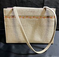 Front view of beige woven rectangular handbag with long shoulder strap and floral embroidery strip near top
