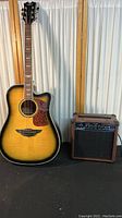 Acoustic-electric guitar sunburst finish with cutaway dreadnought body standing next to wood-cased amplifier