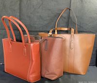 Three handbags displayed standing upright: tan leather tote (Bellucci), brown curved leather handbag (Guias), reddish leather handbag.