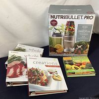 Photo showing new in box NutriBullet Pro blender with 9-piece set, surrounded by four recipe books/binders.