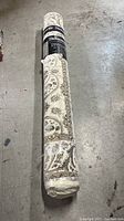 Rolled Thomasville area rug showing part of the ivory, beige, and taupe traditional pattern and product label.