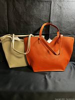 Both vegan leather tote bags shown together, champagne gold and orange bags side by side.
