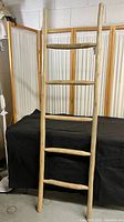 Full view of the wooden decorative ladder standing upright against a black backdrop and white curtain.