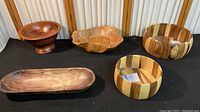 Full view of all five wooden bowls arranged on black cloth showcasing various shapes and finishes.